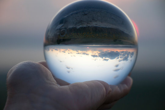 Crystal ball photography - sunset nature landscape, hand holding the ball	