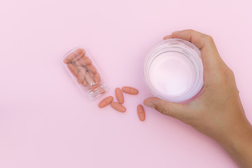 Conceptual flat lay overhead view of woman’s hand with glass of water and many tablets and pills...