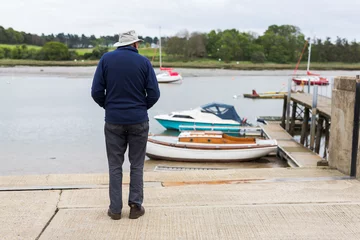 Foto op Canvas A lone retired male standing on the edge of a quay and looking out over the river and the boats that are moored up close by © Collins Photography