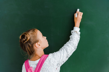 schoolchild holding chalk near chalkboard on green