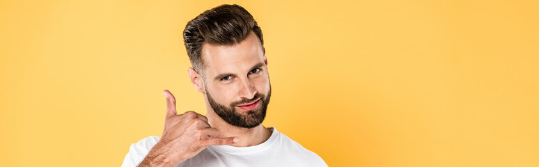 Fototapeta premium panoramic shot of smiling handsome man in white t-shirt showing call me gesture isolated on yellow