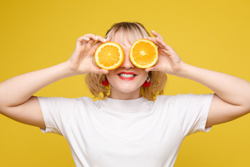 Beautiful model holding an orange. Smiles, makes sponge. Positive photo. Bright makeup. Isolated on yellow background.