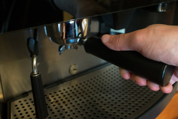 Man's hand holding the portafilter of the coffee machine