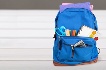 Open blue school backpack on wooden desk background.