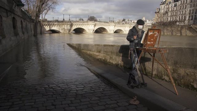 PARIS, FRANCE - CIRCA JANUARY 2018 - A painter near the flooded Seine river with a bridge in the background