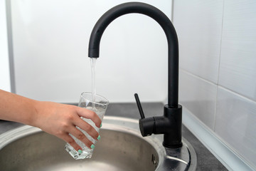 Close up on hands of young woman in the kitchen taking a glass of water at the kitchen sink at home