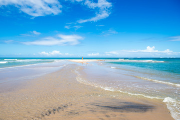 Bright scenic view of shallow waves lapping a bar of golden sand stretching out from an empty Brazilian beach