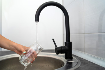 Close up on hands of young woman in the kitchen taking a glass of water at the kitchen sink at home