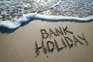 Bank Holiday message handwritten on the smooth sand of an empty beach with oncoming wave
