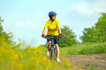 Beautiful girl in yellow riding a bike in nature.
