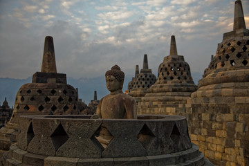 Java, Indonesia - July 24, 2019: Amazing sunrise view of meditating Buddha statue and stone stupas. Ancient Borobudur Buddhist temple. Great religious architecture