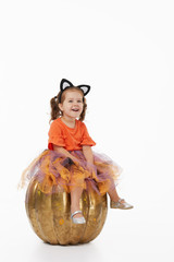Happy Halloween! Cute cheerful little girl  in costume of witch sitting on a big pumpkin isolated on white background