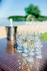 Cold champagne bottle in ice bucket and two glasses of sparkling wine on rattan table near infinity swimming pool
