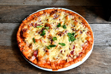 Homemade pizza with cheese, tomatoes, bacon and herbs in a white ceramic plate on a wooden table.