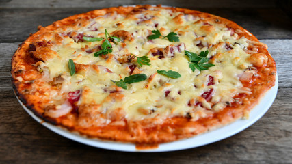 Homemade pizza with cheese, tomatoes, bacon and herbs in a white ceramic plate on a wooden table.