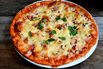 Homemade pizza with cheese, tomatoes, bacon and herbs in a white ceramic plate on a wooden table.