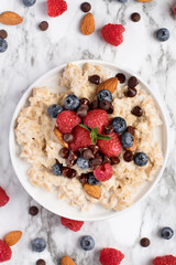 Healthy oatmeal served with berries, chocolate chips, almonds and honey over a marble table background. Shot from top view.