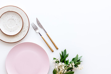 Table setting with plates, fork, knife and flower on white kitchen background top view copy space