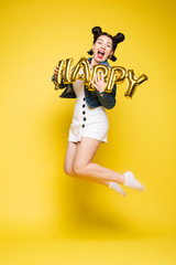 Full length isolate portrait of positive brunette young girl in jeans and t-shirt and sneakers jumping over yellow background. She is smiling at camera.