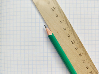 Green pencil and wooden ruler with metric system rests on a white checkered exercise book without notes. School notebook in a cage. Empty notepad with square texture