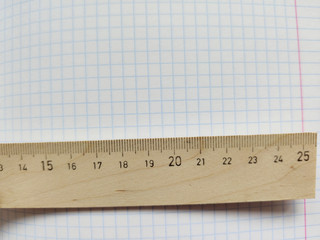 Wooden ruler with metric system rests on a white checkered exercise book without notes. School notebook in a cage. Empty notepad with square texture. Measuring ruler
