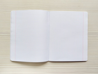 White school notebook in a cage is on a wooden table. Empty notepad is on a desk. Exercise book...