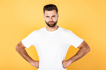 smiling handsome man in white t-shirt with hands on hips isolated on yellow