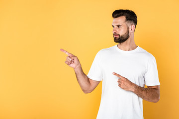 handsome man in white t-shirt pointing with fingers aside isolated on yellow