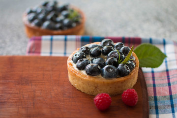 Tartlets with blueberries on the wooden board with a checkered napkin, with fresh berries of raspberry. Top view