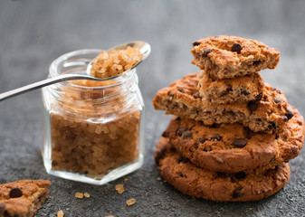 Freshly baked chocolate cookies and a glass jar with brown sugar on a grey table