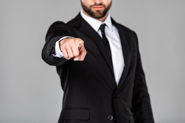cropped view of businessman in black suit pointing with finger at camera isolated on grey