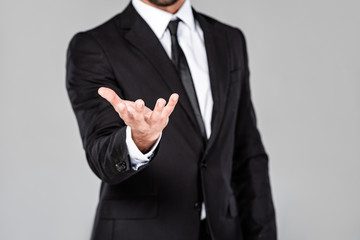 partial view of businessman in black suit with begging hand isolated on grey