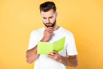 thoughtful handsome man in white t-shirt reading book isolated on yellow