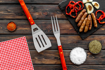 Barbecue with sausages, vegetables on kitchen board and spices on wooden background top view