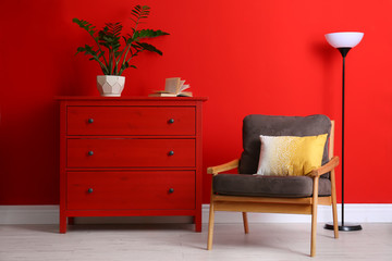 Stylish room interior with modern furniture and houseplant near red wall
