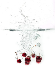 fresh cherries falling in water on a white background 