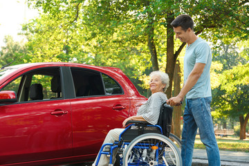 Young man with disabled senior woman in wheelchair near car outdoors