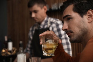 Young man with glass of whiskey in bar. Space for text