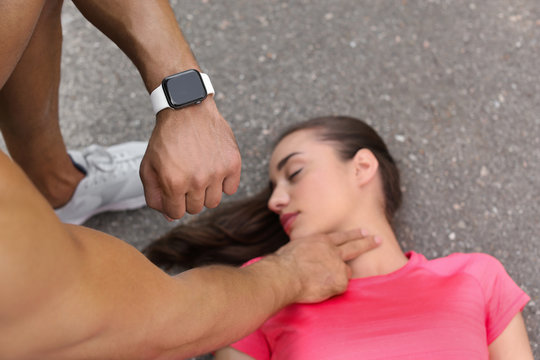 Young man checking pulse of unconscious woman on street