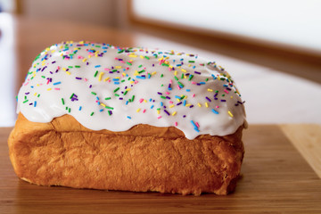 Paska loaf on a wooden cutting board covered in icing and sprinkles; colorful sprinkles on top of iced Easter bread