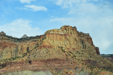 Multicolored rock layers on display at Capitol Reef National Park, peaks and rock structures against a powdery blue sky