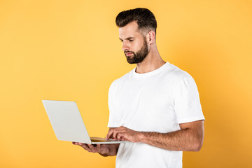 man in white t-shirt using laptop isolated on yellow