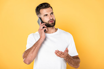 handsome man in white t-shirt talking on smartphone isolated on yellow