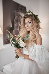 Naklejka premium The bride's fees at the hotel. A beautiful blonde is standing at the window in a wedding dress. Photo with a bouquet.