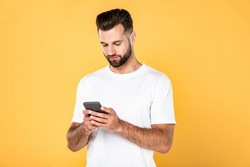 handsome man in white t-shirt using smartphone isolated on yellow