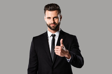 smiling handsome businessman in black suit showing thumb up isolated on grey