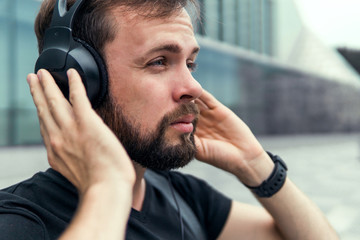 Young successful entrepreneur going for a business meeting, handsome man listening music in headphones, street photo, beard face, outdoor hipster portrait, iwatch in hand, sport, USA city, brutal