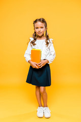 smiling and cute kid holding books and standing on orange