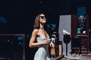 A beautiful girl in a beige jacket drinks coffee from a glass talking on the phone, wearing sunglasses works in the office in the business center, the manager, the employee of the company, happy face