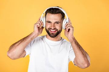 happy man in white t-shirt listening music in headphones isolated on yellow